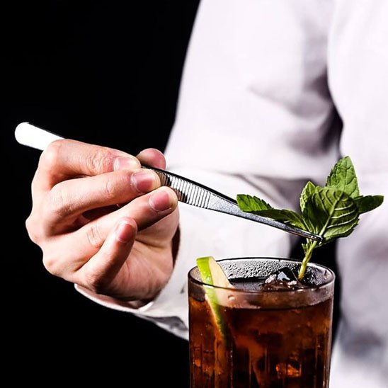 Une pince déposant une branche de menthe dans du thé