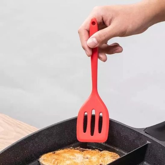 main qui tient une spatule rouge dans une poêle