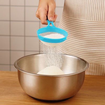 passoire bleu filtrant de la farine dans un bol