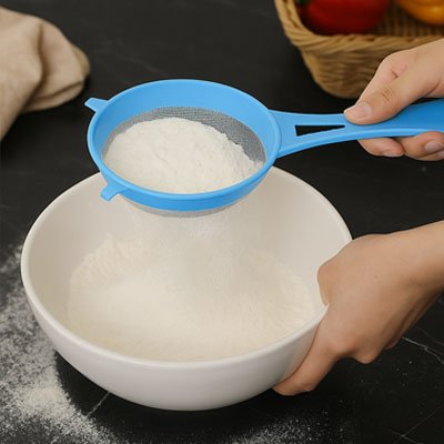 passoire bleue filtrant dans un bol blanc