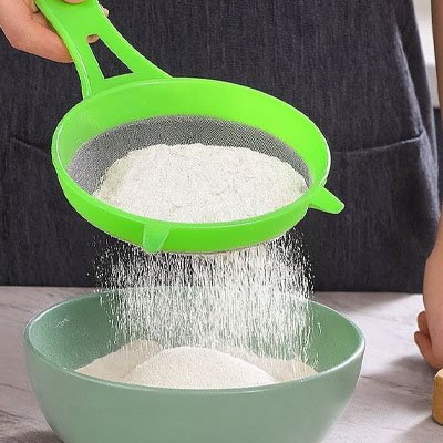 passoire verte filtrant de la farine dans un saladier 
